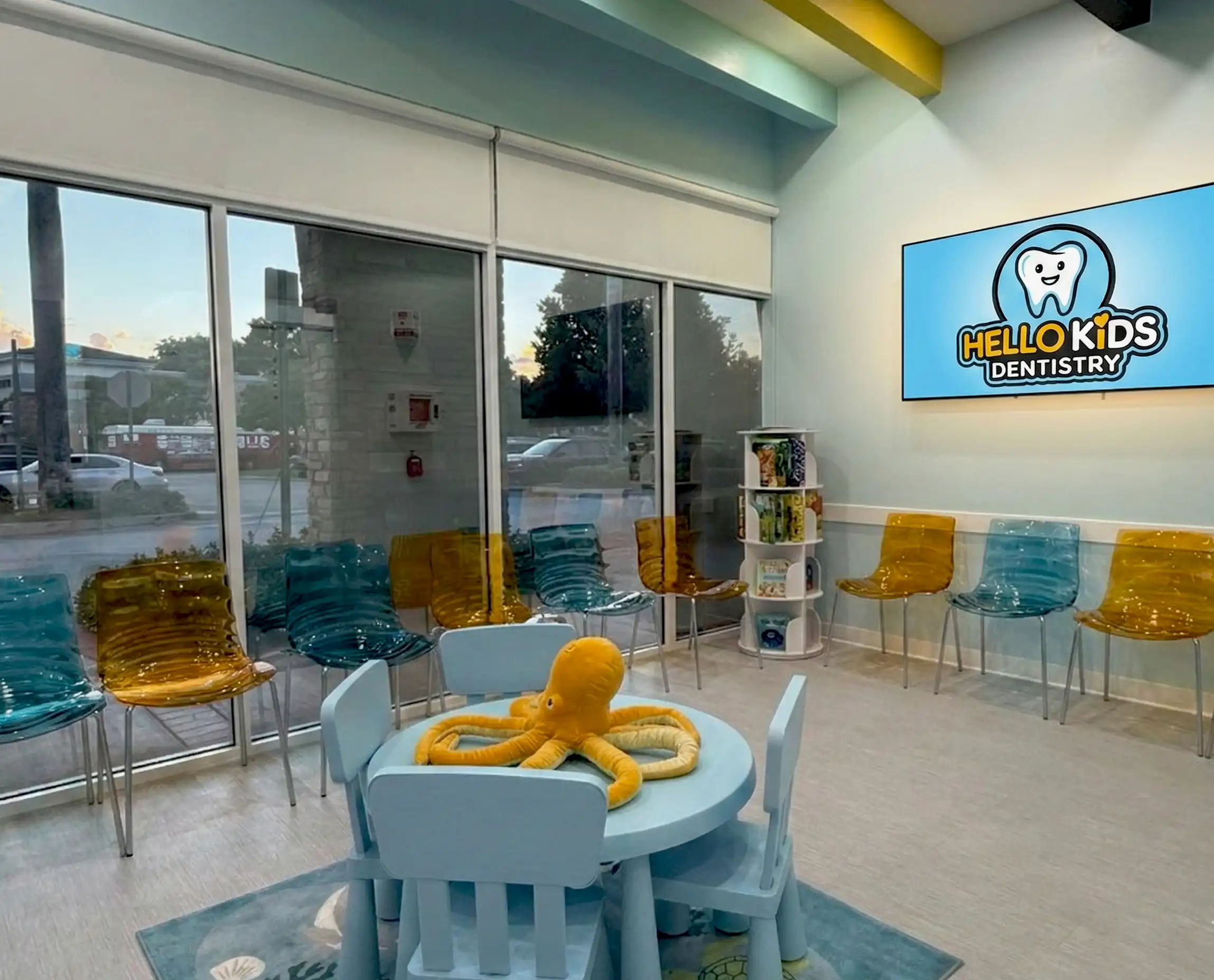 The modern and welcoming waiting room at Hello Kids Dentistry Pediatric Dentist in Pembroke Pines, FL, featuring a branded screen and a fun play area for kids dental care.